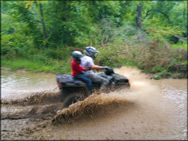 Adult and small child on ATV going through water crossing.