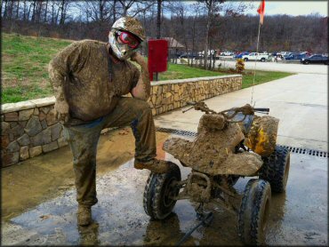 Rider and Suzuki ATV with orange whip flag covered in mud.