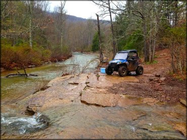 UTV with cooler parked on rocky ledge alongside creek.