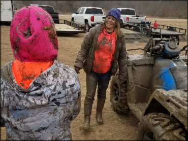 Two young women wearing winter clothing covered in mud standing next to ATV.