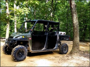 Green Polaris Ranger Crew UTV with winch attached to front bumper and mud tires parked alongside trail.