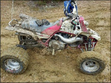 Yamaha Banshee covered in mud with pair of riding gloves on seat, blue HJC motorcycle helmet and goggles on handle bars.
