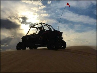 Polaris side by side with orange safety flag parked on top of sand dune.