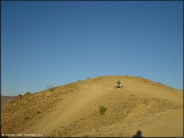 Man on Suzuki RM250 riding down short hill.
