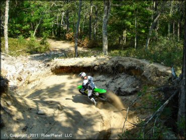 Man on Kawasaki four-stroke going through deep sand berm on motocross track.