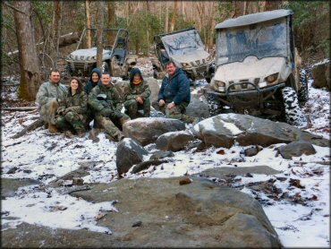 Three Polaris Rangers, four men and two women in camouflage riding gear posing for photo.