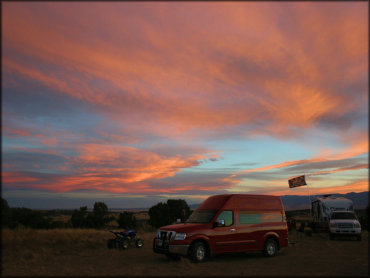 Yamaha Raptor ATV parked next to red van and travel trailer.