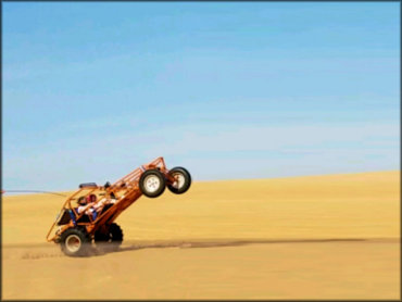Dune buggy with two passengers popping a wheelie in the sand.