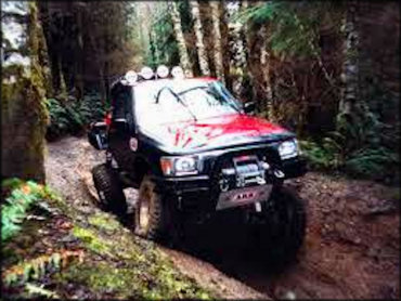 Modified 4x4 truck with a winch on the front bumper and KC lights navigating a deep rut.