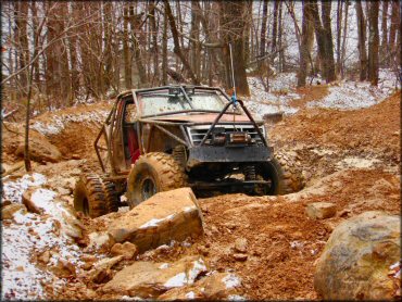 Modified 4x4 truck with big mud tires, roll cage, heavy duty bumper with winch going up muddy and rocky trail.