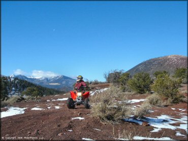 Woman on Honda TRX 250EX parked with snow capped mountains in the background.