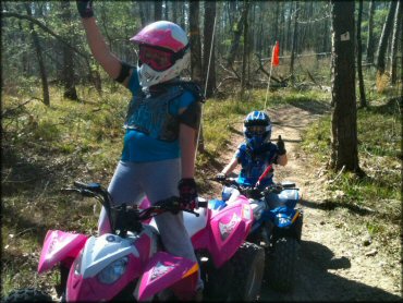 Young girl on pink ATV and small boy on blue ATV navigating easy trail.