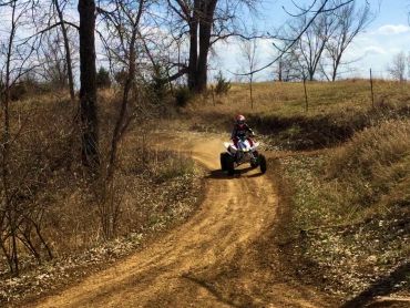 Woman on ATV riding around kids motocross track.