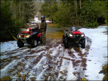Two ATVs with man wearing camouflage riding gear on trail.