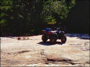 Blue four wheeler with camping gear parked on large flat rock.