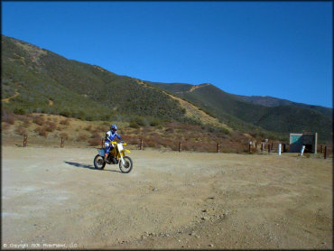 Young woman wearing Acerbis motocross gear riding RM-250 two-stroke dirt bike around staging area.