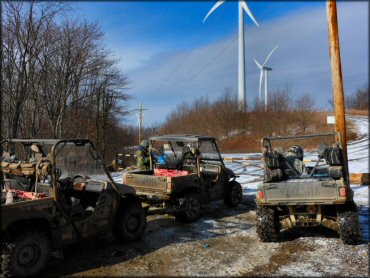 Three Yamaha Rhino side by sides parked behind gate near wind turbine farm.