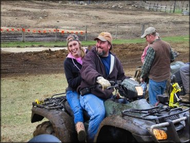 Man and woman sitting on a dark green Honda ATV.