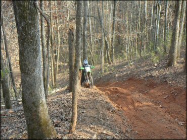 Man on Kawasaki dirt bike trying to go up steep and rutted ATV trail.