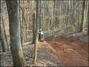 Man on Kawasaki dirt bike trying to go up steep and rutted ATV trail.