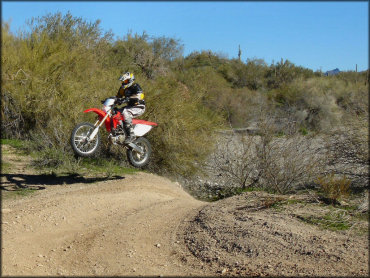 Man on Honda CRF250X dirt bike getting a little jump off an ATV trail.