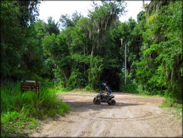 Man wearing backpack on mud covered ATV heading into campground.