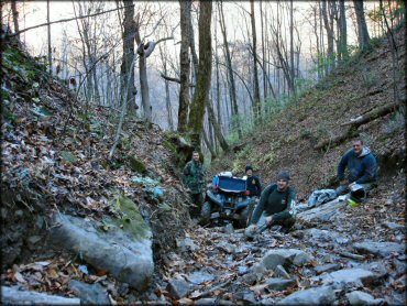 Group photo of four young men standing next to ATV carrying camping gear and winch on front bumper.