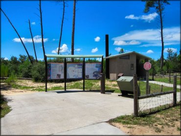 Photo of vault toilet, trash receptacles and informational kiosk with trail maps and a self pay kiosk.