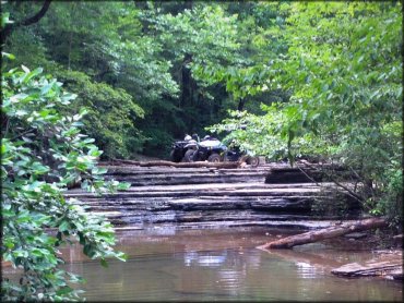 A close up photos of two ATVs parked on rocky ledge overlooking shallow stream.