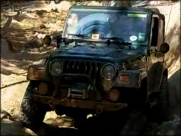 Dark green 4x4 Jeep Wrangler with a winch on the front bumper navigating large rocks.