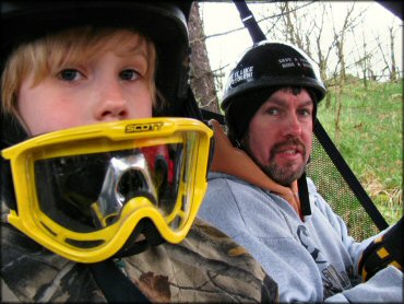 A Yound Father and Son Riding in a UTV Wearing Helmets and Goggles