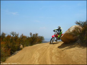 Honda CRF250X going past large boulder on the trail.