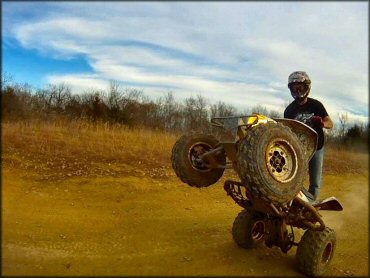 Young man on ATV popping a wheelie down dirt trail.