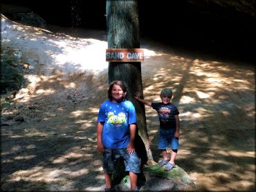 Two young kids standing in front of tree with trail signage.