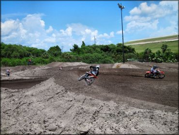 Two Honda dirt bikes going through berm on motocross track.