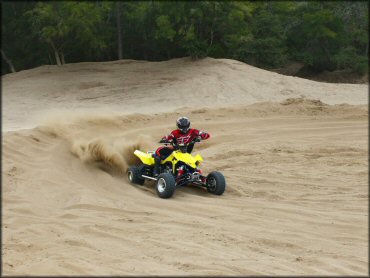 Man wearing Fly Racing black and red riding gear on Suzuki QuadSport going through sandy berm.