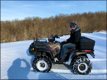 Man sitting on top of parked Polaris 700 Sportsman ATV with snow tires and rear cargo box.