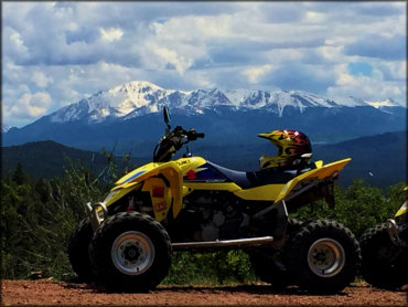 Suzuki ATV parked with motorcycle helmet on seat with scenic view Rocky Mountains in the background.