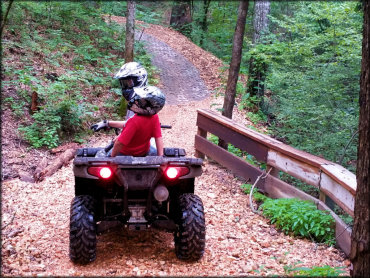 Two riders on quad going down small hill wearing helmets and ANSR goggles.