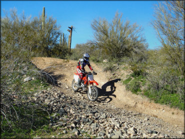 A rider wearing Fox motocross gear riding a Honda CRF150R going through a rocky section on ATV trail.