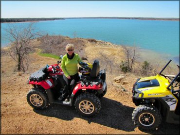 Mature woman sitting on Polaris Sportsman 850 with front storage box parked next to Polaris RZR 800.