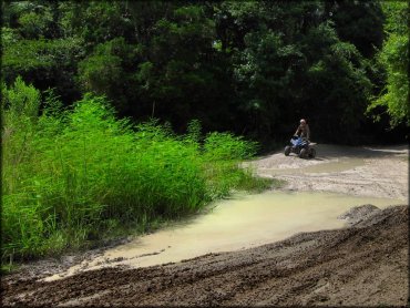 Young man on ATV going through some mud puddles.