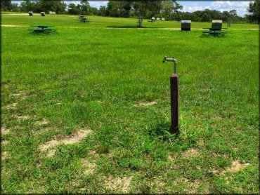 Water spigot surrounded by picnic tables and trash receptacles.