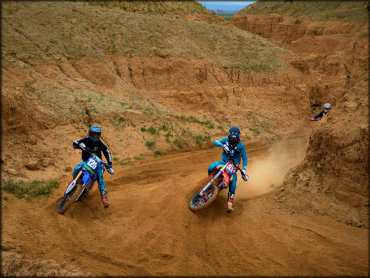 Three Motocross Bikes Railing a Small Berm in a Narrow Canyon