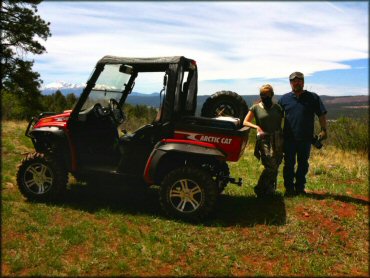 Man and woman standing next to Red Arctic Cat Prowler X12 with Maxxis Bighorn tires.