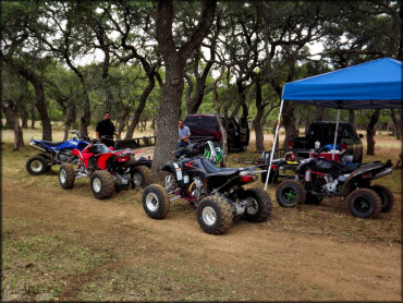 Some ATVs and trucks parked under the trees in the staging area.