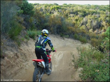 Woman wearing black and green Fox motocross gear riding Honda CRF150F on ATV trail.