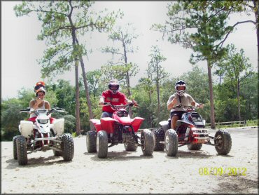 Three young men wearing helmets sitting on ATVs.
