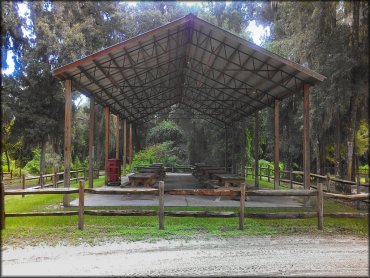 Large outdoor gazebo on concrete slab with ten picnic tables.