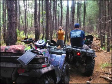 Young man standing alongside trail with camera taking group photo riders on ATVs.